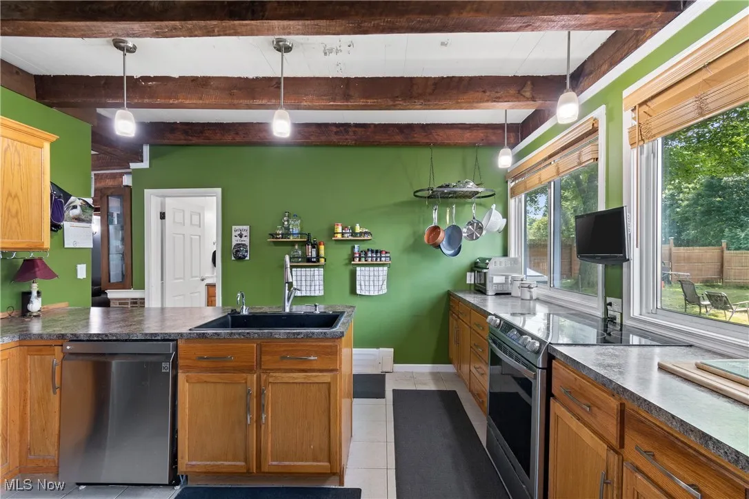 Kitchen with stainless steel electric range, a peninsula, dishwashing machine, dark countertops, and beamed ceiling