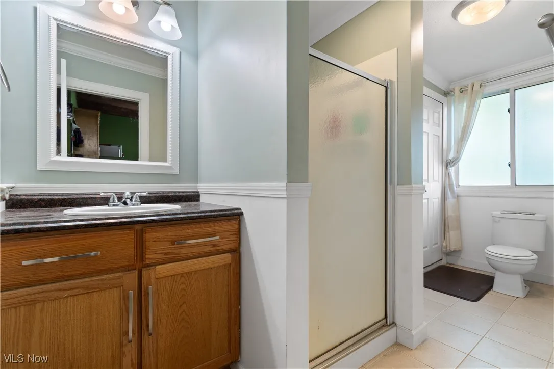 Full bath featuring ornamental molding, a shower stall, vanity, tile patterned floors, and a wainscoted wall