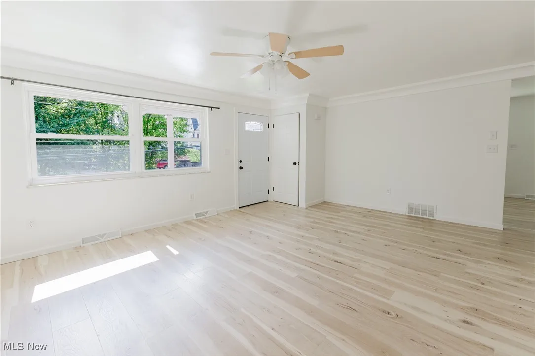 Unfurnished room featuring a ceiling fan, light wood-style flooring, and ornamental molding