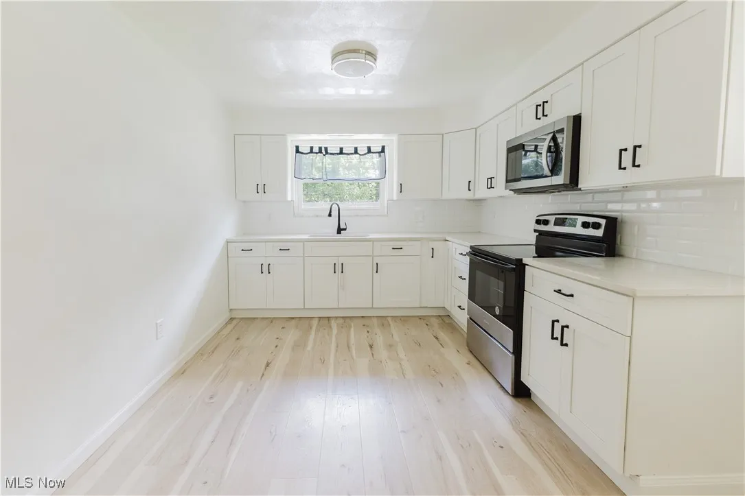 Kitchen featuring stainless steel appliances, decorative backsplash, white cabinetry, light wood-style flooring, and light countertops