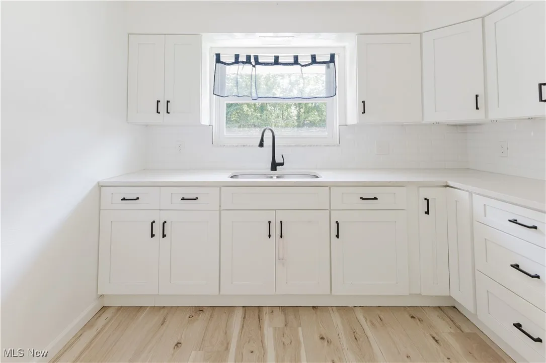 Kitchen featuring tasteful backsplash, white cabinets, light wood-type flooring, and light countertops