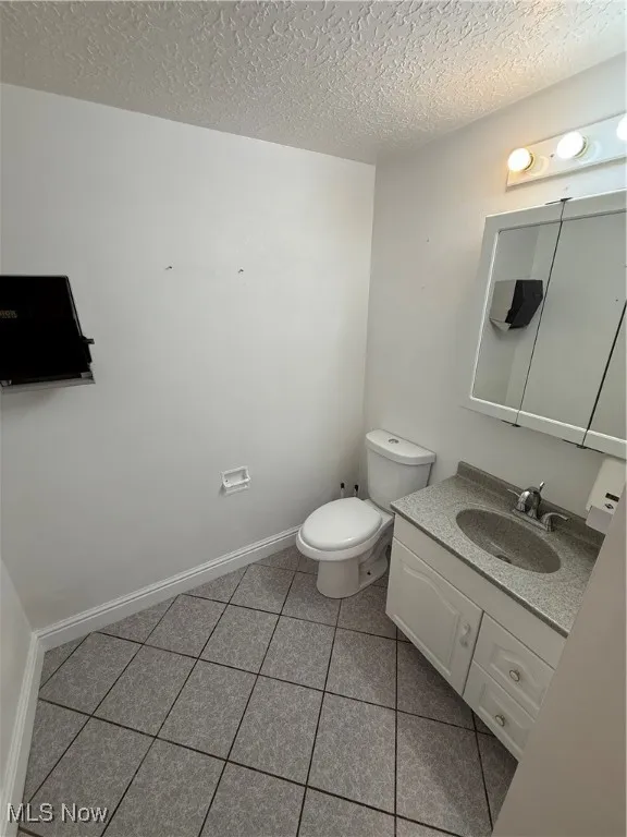 Half bathroom featuring vanity, a textured ceiling, and tile patterned floors