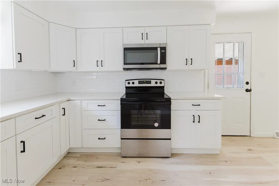 Kitchen featuring stainless steel appliances, light wood-style floors, backsplash, and white cabinetry