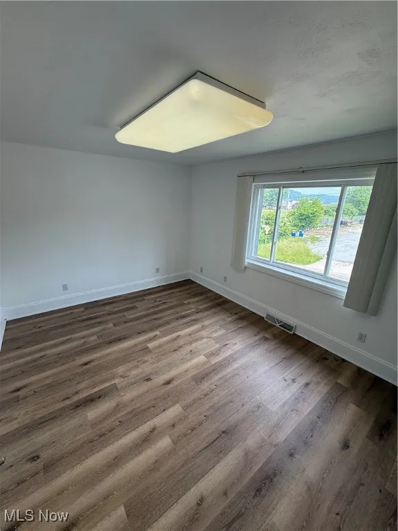 Unfurnished room with baseboards and dark wood-type flooring