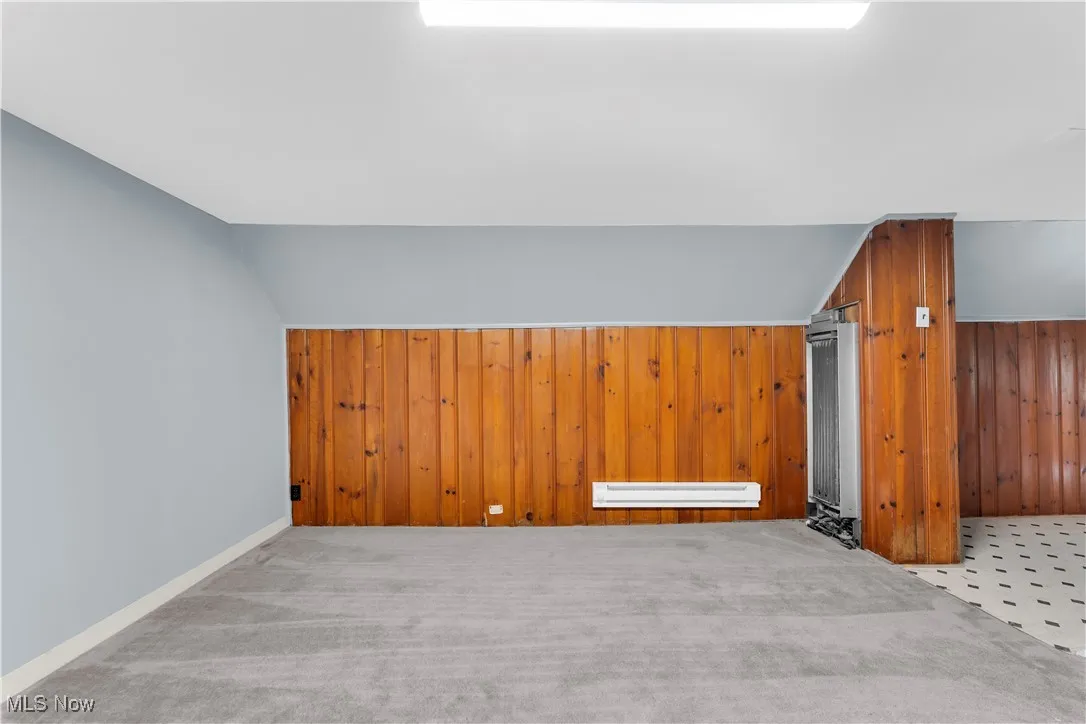 Additional living space with wood walls, carpet, a baseboard heating unit, and vaulted ceiling