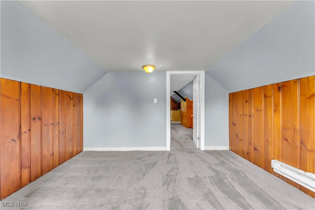 Additional living space with wood walls, carpet floors, baseboard heating, and lofted ceiling