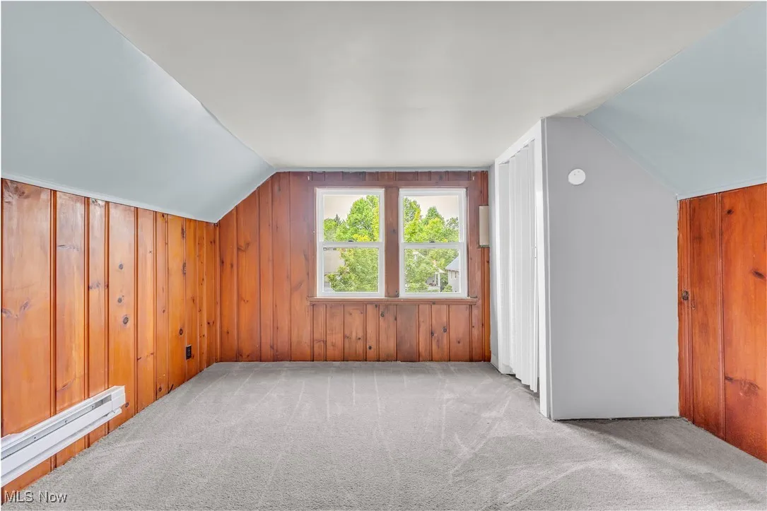 Bonus room featuring lofted ceiling, carpet, a baseboard radiator, and wood walls