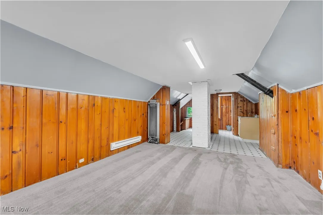 Bonus room featuring wooden walls, lofted ceiling, carpet flooring, and a baseboard radiator