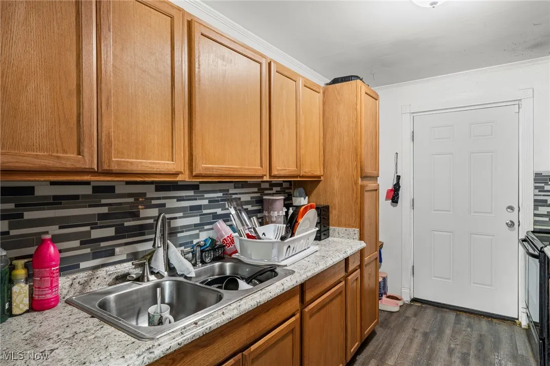 Kitchen with backsplash, light countertops, electric range, dark wood-style floors, and brown cabinets