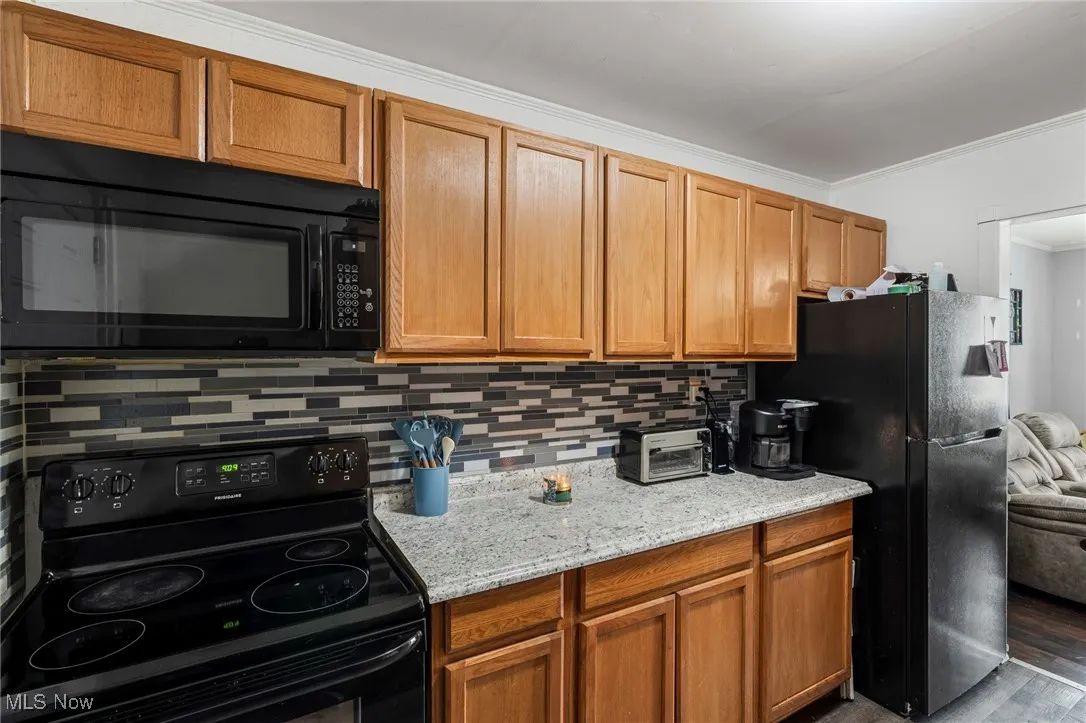 Kitchen featuring black appliances, ornamental molding, backsplash, light stone countertops, and wood finished floors