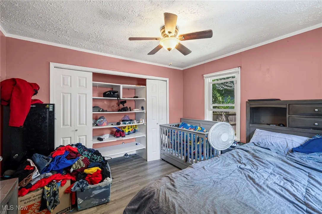 Bedroom featuring a textured ceiling, crown molding, wood finished floors, ceiling fan, and a closet