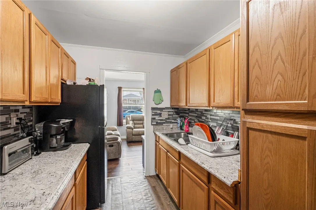 Kitchen with crown molding, backsplash, freestanding refrigerator, wood finished floors, and light stone counters