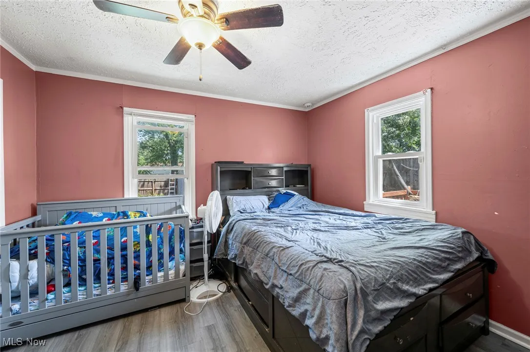 Bedroom featuring wood finished floors, a textured ceiling, crown molding, and ceiling fan