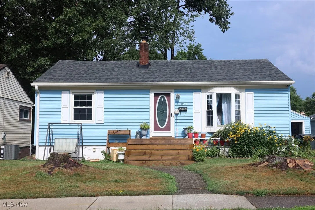 View of front facade featuring a chimney, roof with shingles, and a front yard