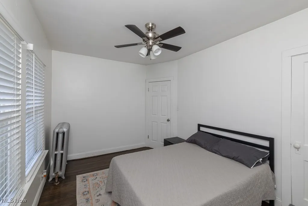 Bedroom featuring dark wood finished floors, radiator, multiple windows, and a ceiling fan