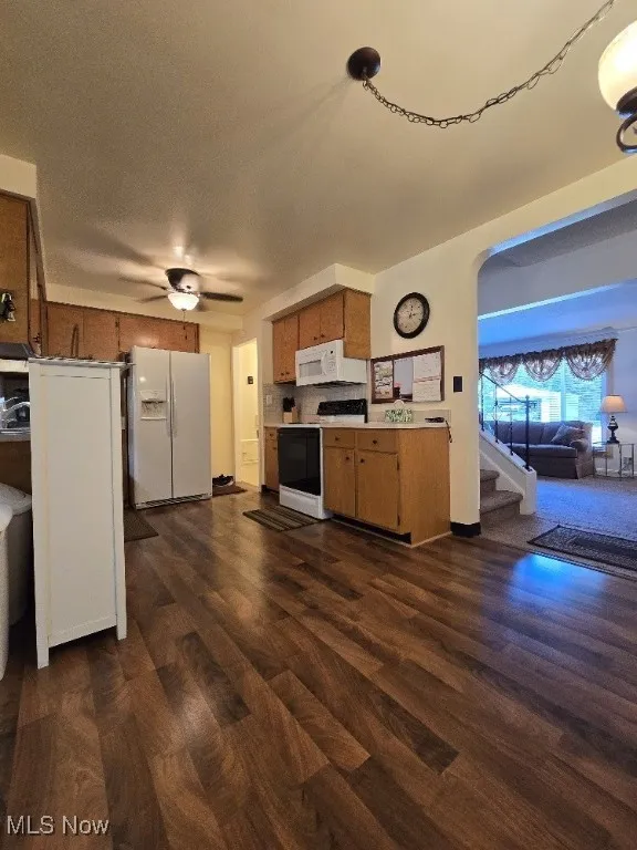 Kitchen featuring white appliances, brown cabinetry, light countertops, dark wood-type flooring, and a ceiling fan