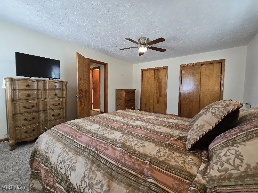 Carpeted bedroom with two closets, a textured ceiling, and a ceiling fan