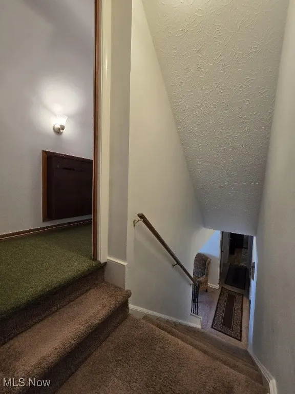 Stairway featuring carpet flooring, a textured ceiling, and vaulted ceiling