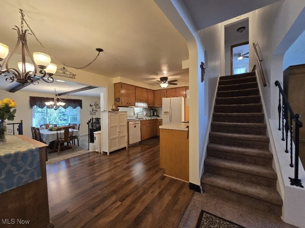 Kitchen featuring a ceiling fan, a chandelier, light countertops, brown cabinets, and dark wood-type flooring