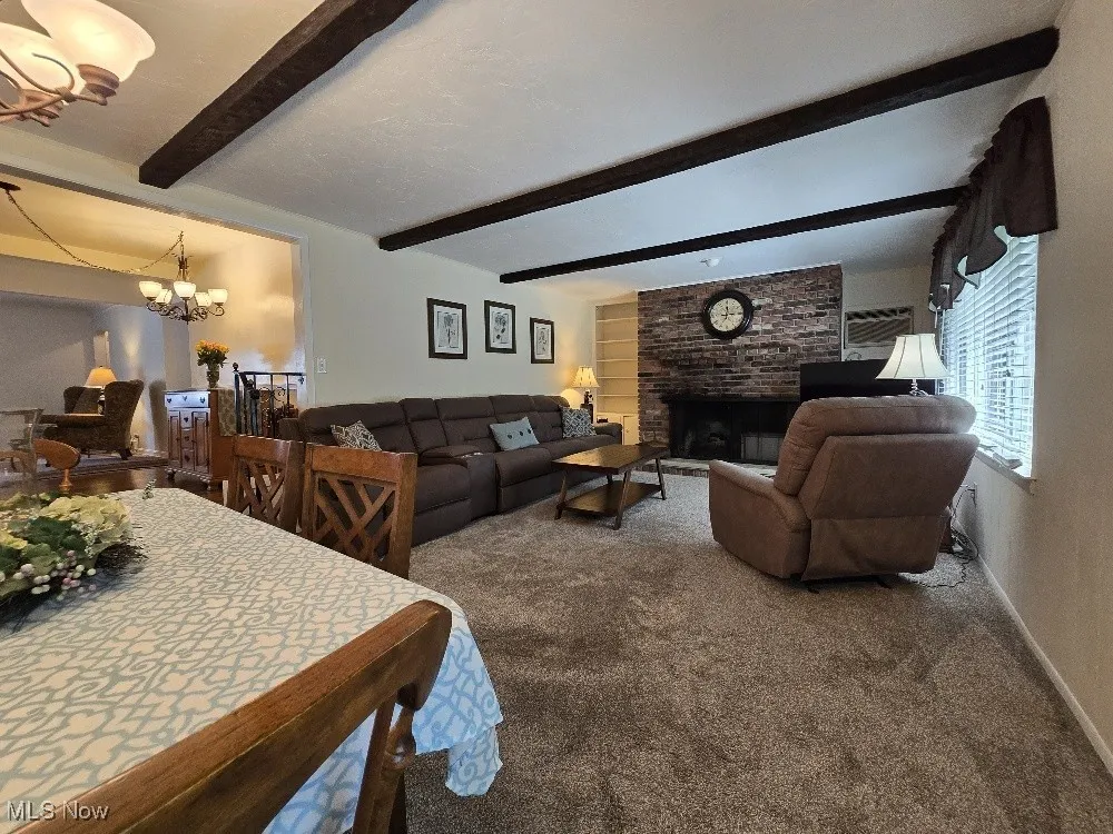 Living room with a chandelier, carpet, beamed ceiling, and a brick fireplace