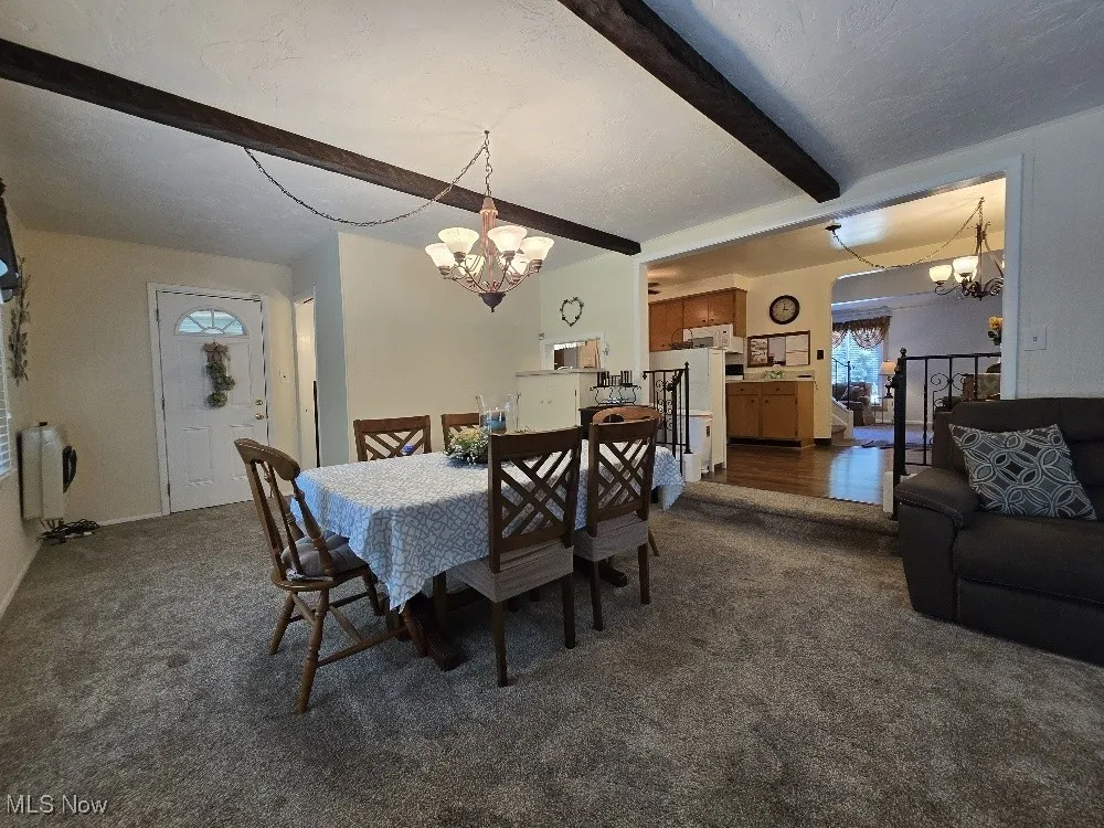 Dining area featuring a chandelier, beam ceiling, carpet flooring, heating unit, and a textured ceiling