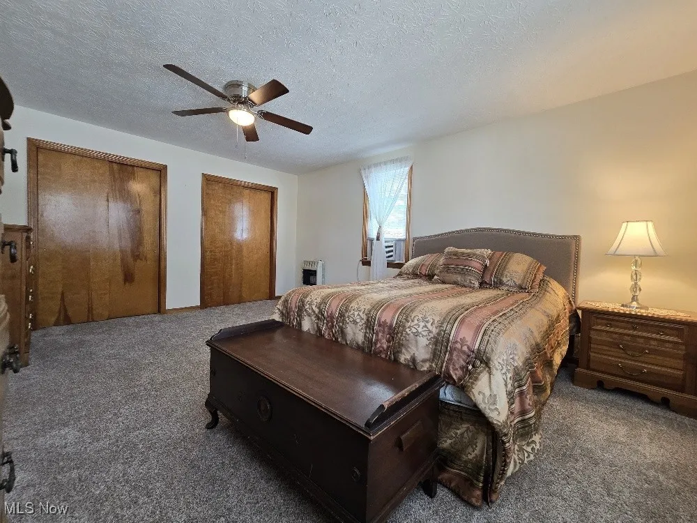 Carpeted bedroom featuring a textured ceiling, multiple closets, ceiling fan, and heating unit