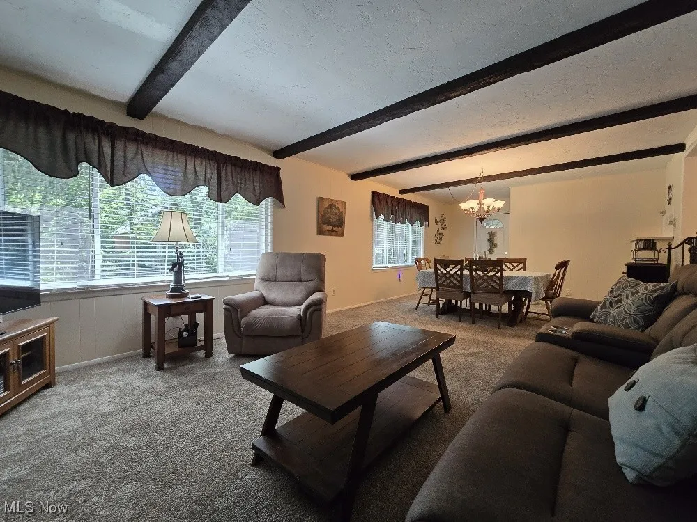 Carpeted living area with beam ceiling, a chandelier, and a textured ceiling