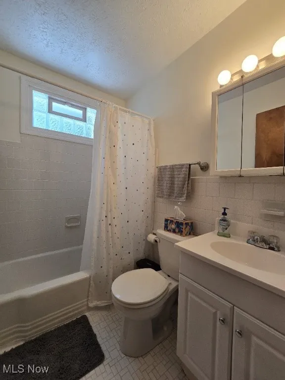 Full bath featuring tile walls, vanity, a textured ceiling, and shower / bathtub combination with curtain
