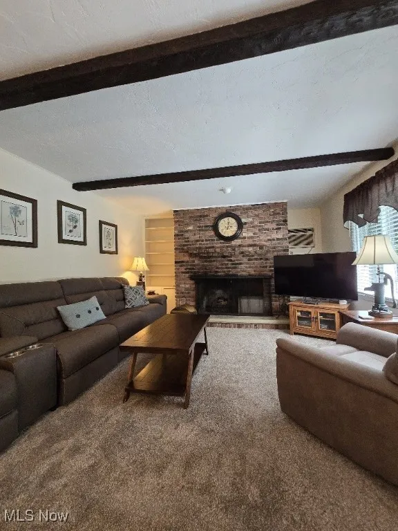 Living area with carpet flooring, beamed ceiling, a fireplace, and a textured ceiling