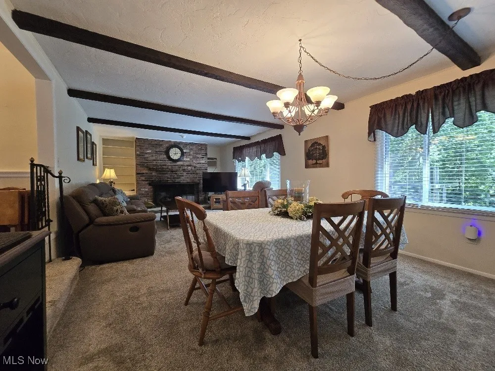 Carpeted dining area featuring beamed ceiling, a textured ceiling, a chandelier, and a large fireplace