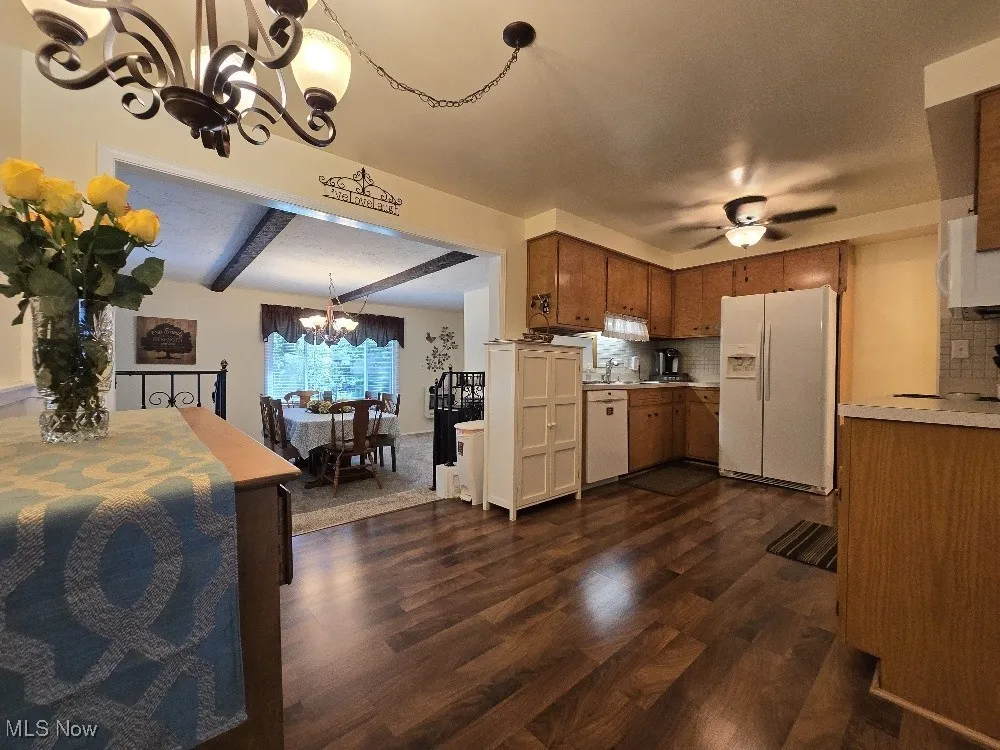 Kitchen featuring a chandelier, beamed ceiling, white appliances, dark wood-type flooring, and light countertops