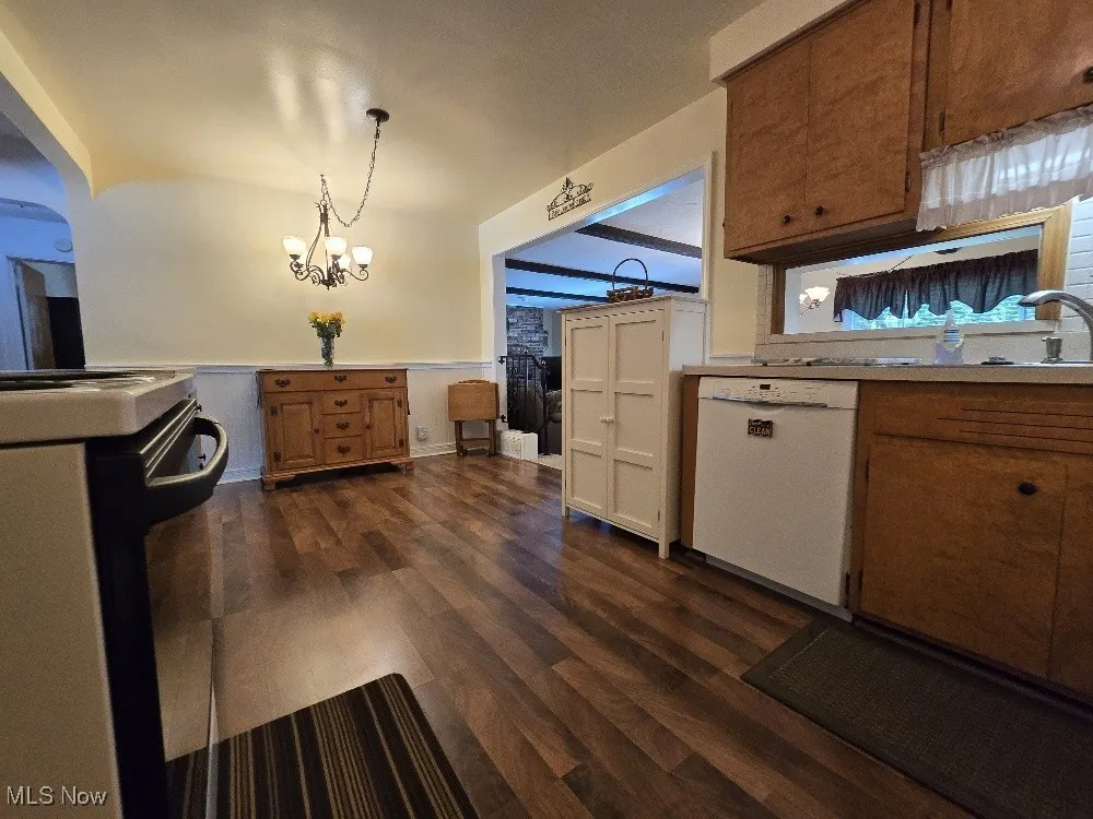 Kitchen featuring dishwasher, wainscoting, brown cabinets, light countertops, and a chandelier