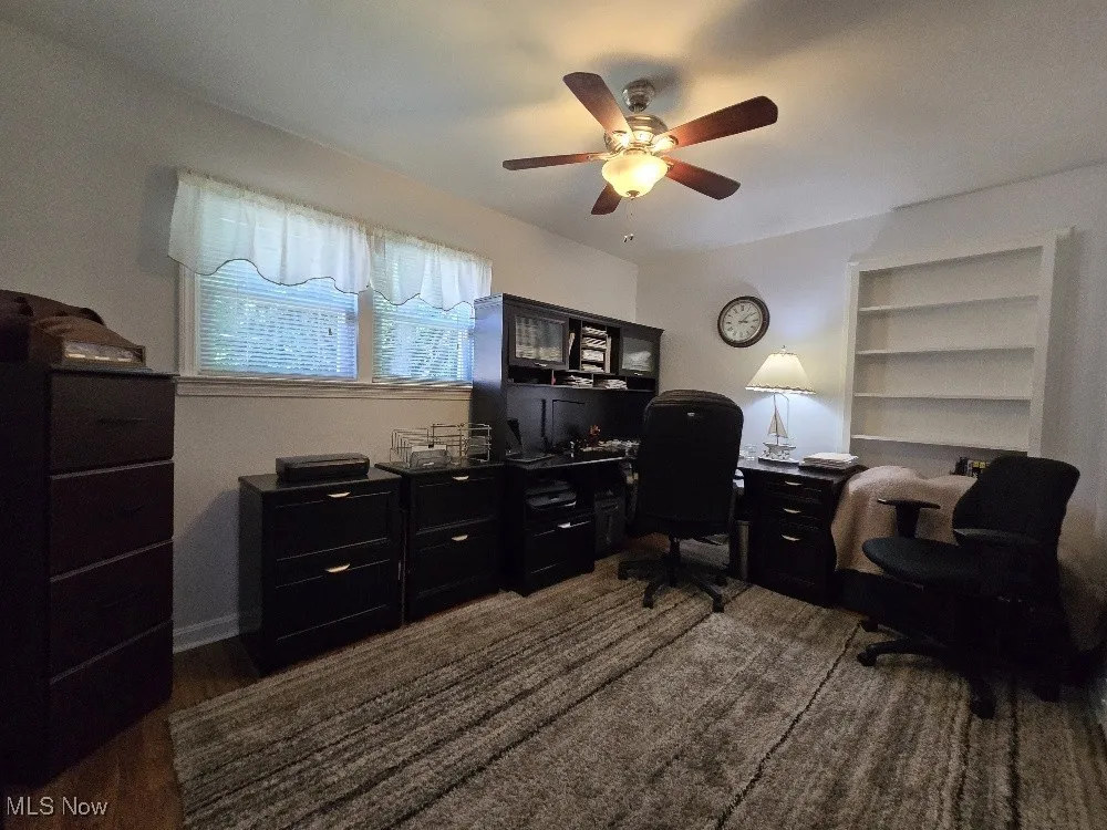 Office space with ceiling fan, built in shelves, and dark wood-type flooring