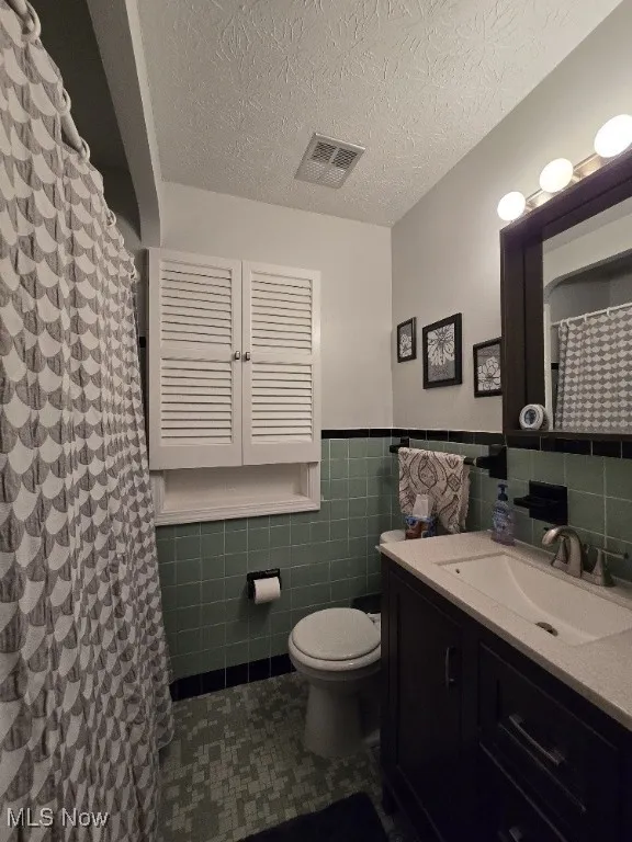 Full bath featuring a textured ceiling, vanity, tile walls, a wainscoted wall, and a shower with shower curtain