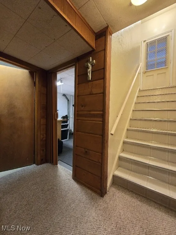 Stairway with carpet, wooden walls, and a drop ceiling