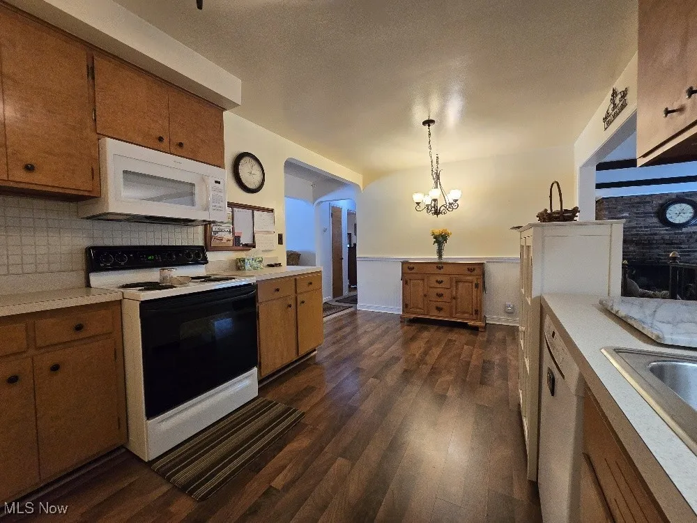 Kitchen featuring white appliances, brown cabinetry, light countertops, wainscoting, and a chandelier