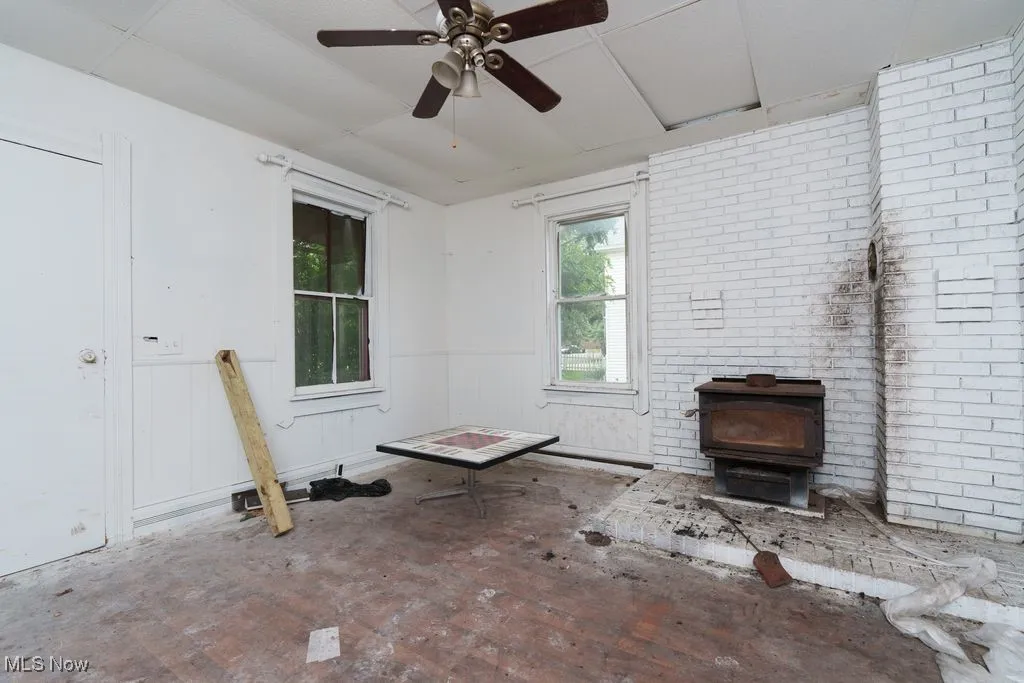 Unfurnished living room with a wood stove, a ceiling fan, and wainscoting
