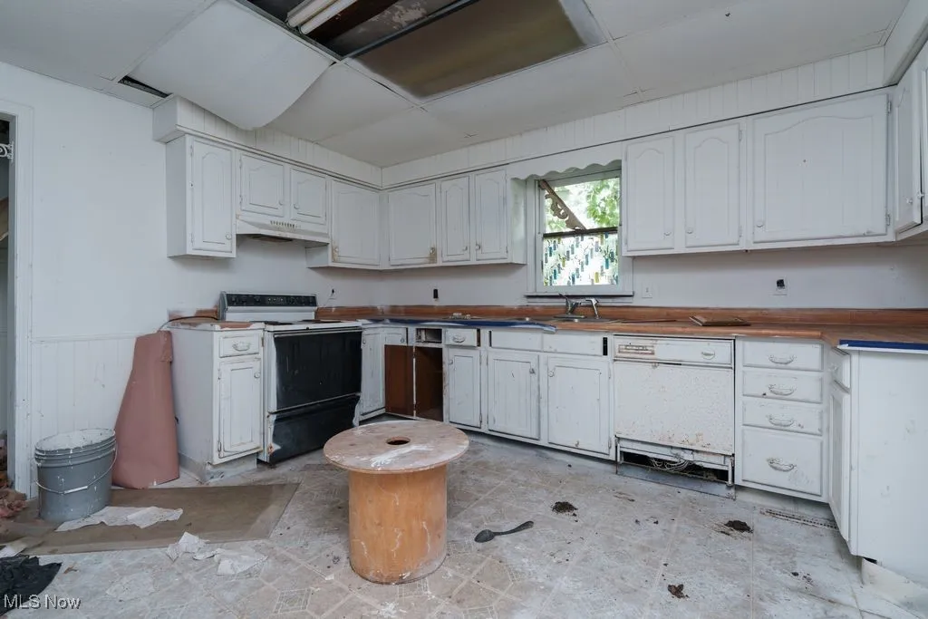 Kitchen featuring white appliances, a wainscoted wall, and white cabinets