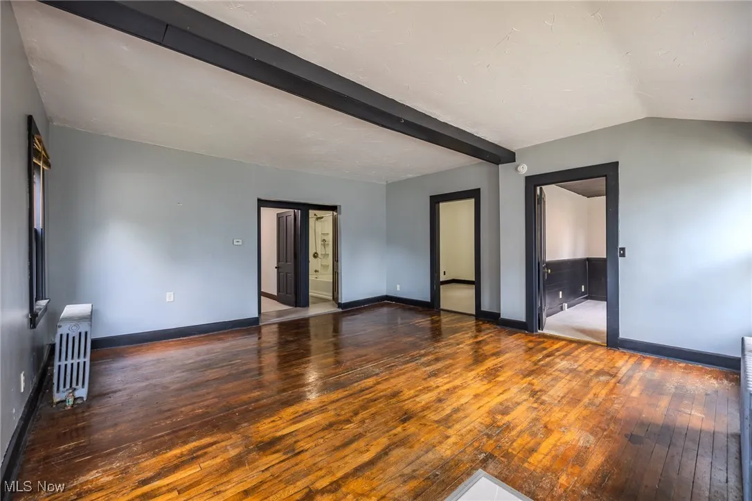 Unfurnished living room featuring hardwood / wood-style floors, beamed ceiling, and radiator