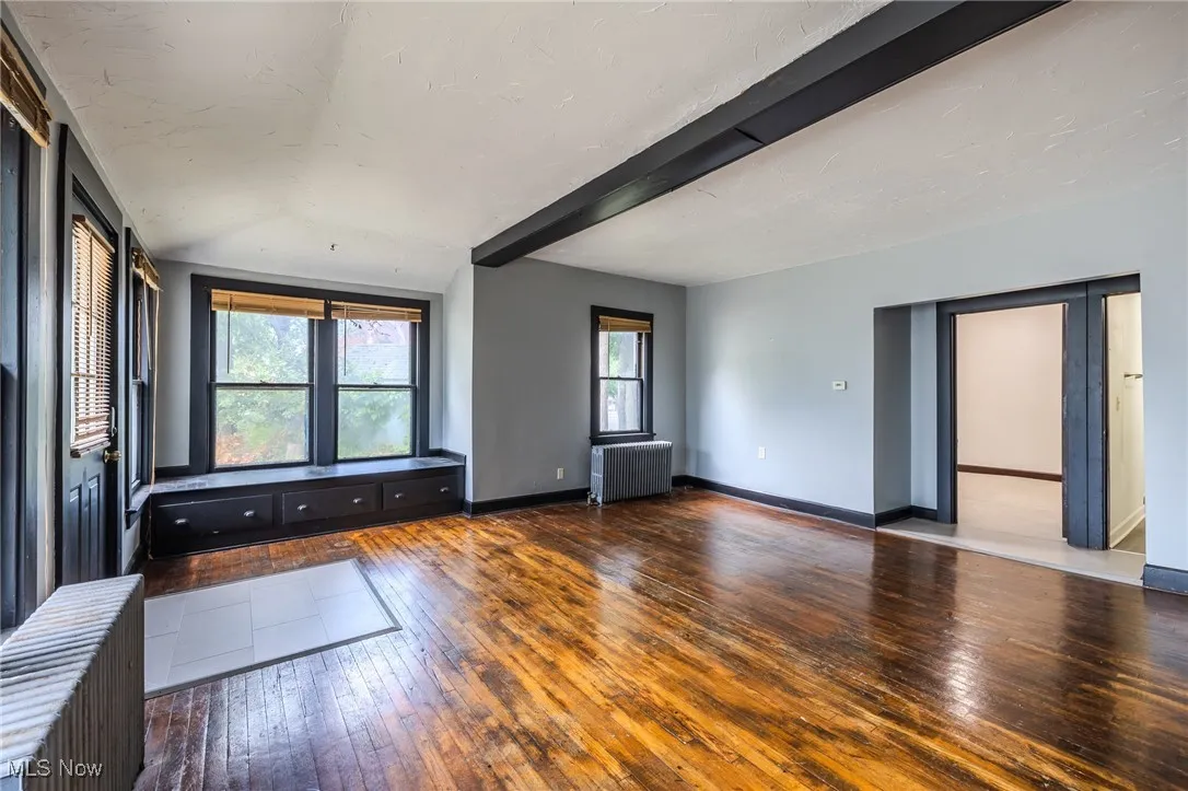 Empty room with hardwood / wood-style floors, beamed ceiling, and radiator heating unit