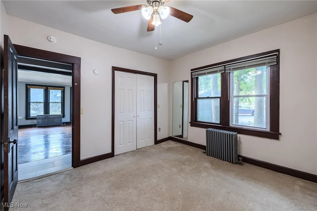 Unfurnished bedroom with carpet floors, radiator heating unit, ceiling fan, and a closet