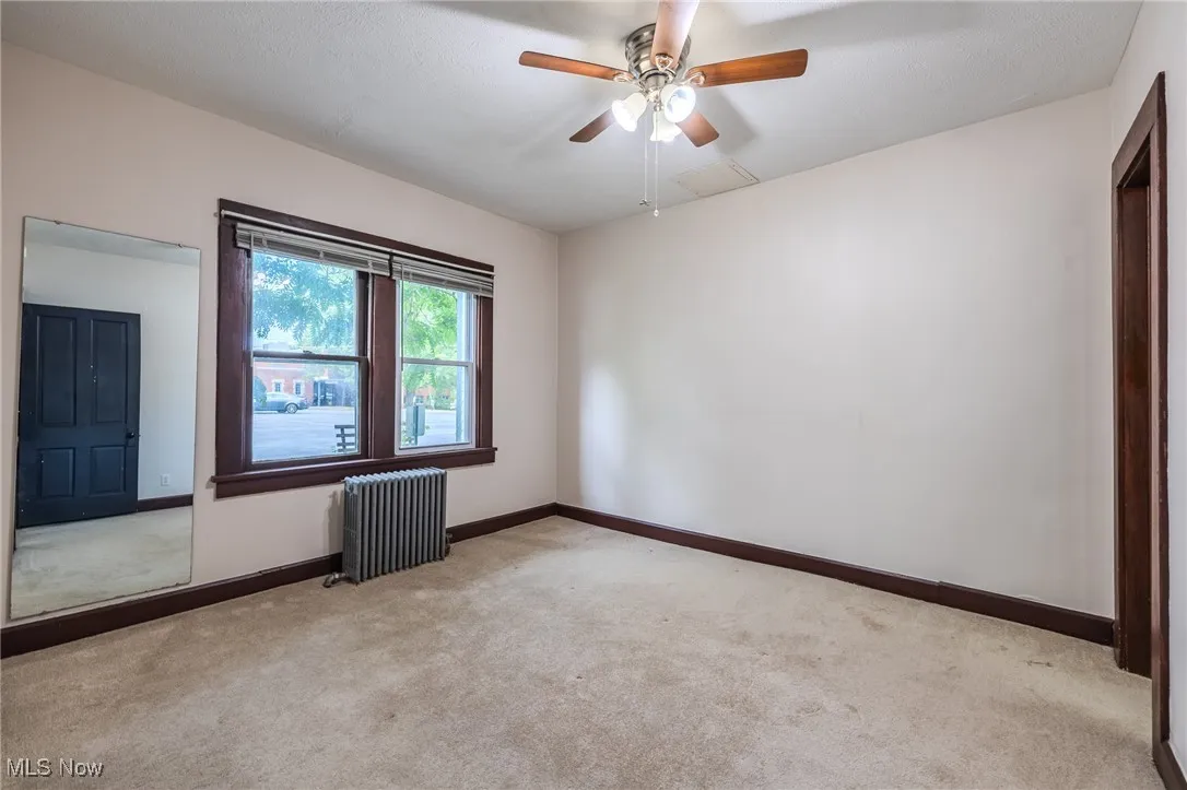 Carpeted empty room featuring radiator heating unit and ceiling fan