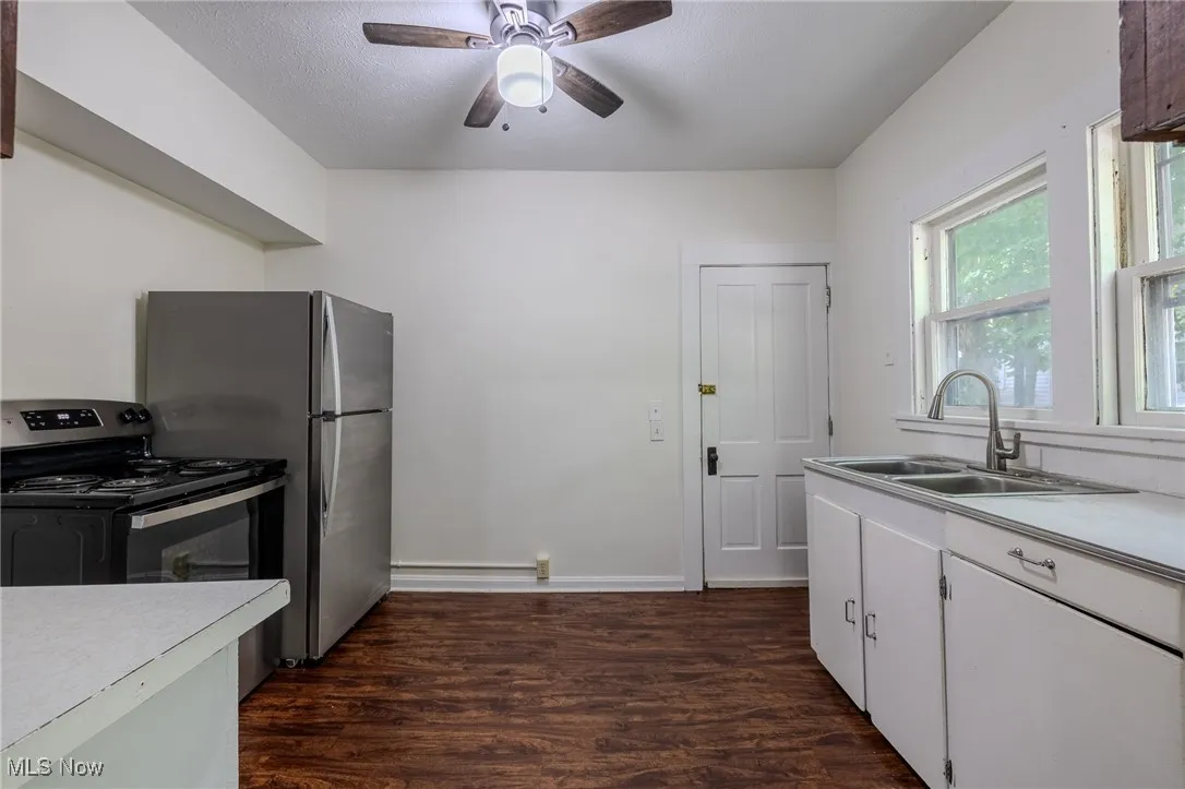 Kitchen with stainless steel appliances, dark wood-style flooring, light countertops, and a ceiling fan