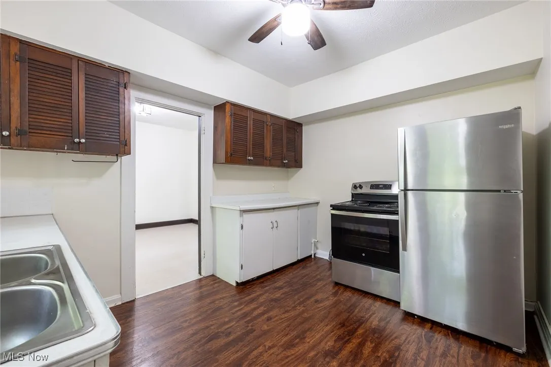 Kitchen with appliances with stainless steel finishes, light countertops, ceiling fan, and dark wood-type flooring
