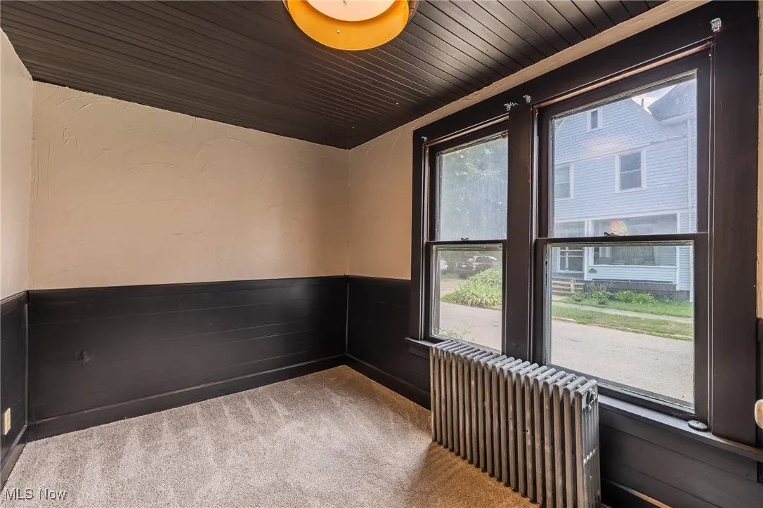 Empty room featuring radiator, carpet floors, wainscoting, and wood ceiling