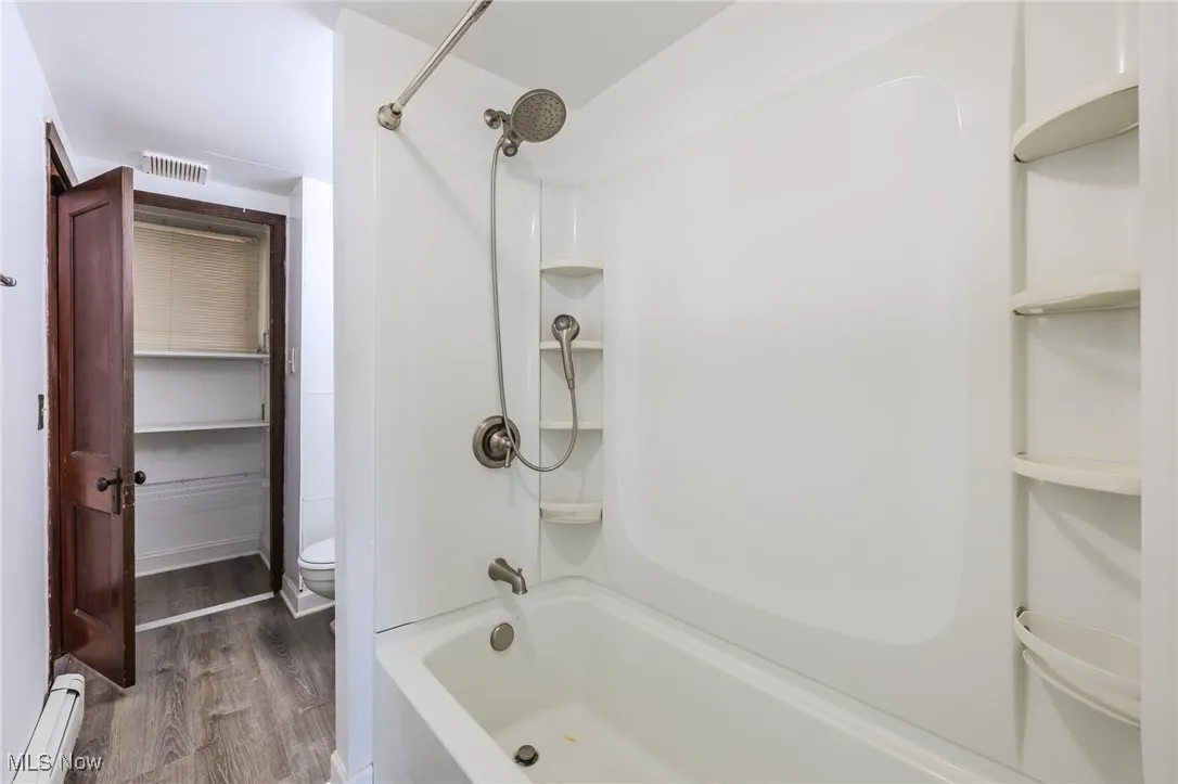 Bathroom with a baseboard heating unit, washtub / shower combination, and wood finished floors