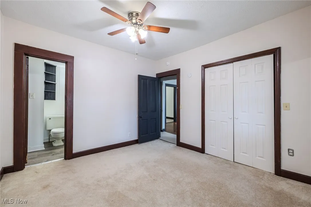Unfurnished bedroom with light colored carpet, a closet, a ceiling fan, and connected bathroom