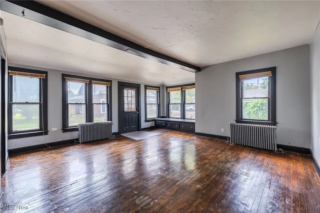 Unfurnished living room with wood-type flooring, radiator heating unit, and beamed ceiling