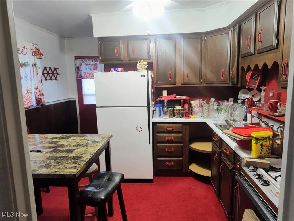 Kitchen featuring freestanding refrigerator, light countertops, gas range oven, and dark carpet