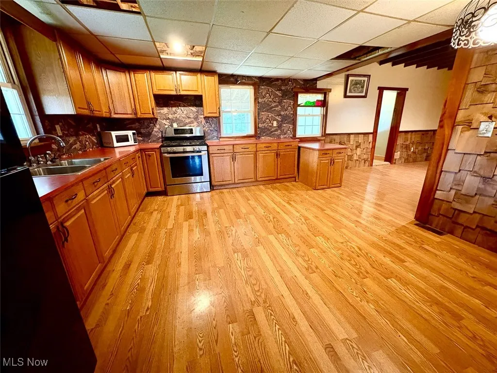 Kitchen featuring wainscoting, gas range, light wood finished floors, brown cabinets, and a drop ceiling